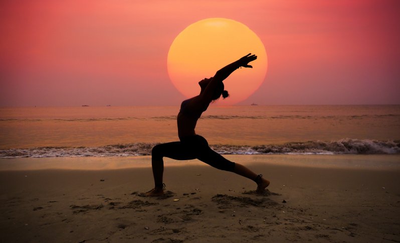 Žena cvičiaca jogu na pláži pri mori pri západe slnka.